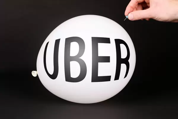 Hand uses a needle to burst a balloon with UBER text