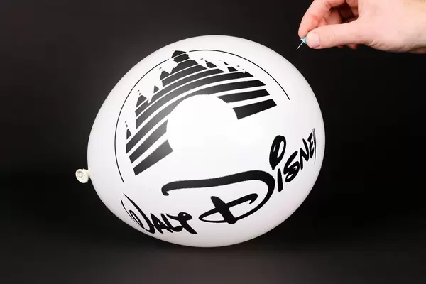 Hand uses a needle to burst a balloon with Walt Disney logo