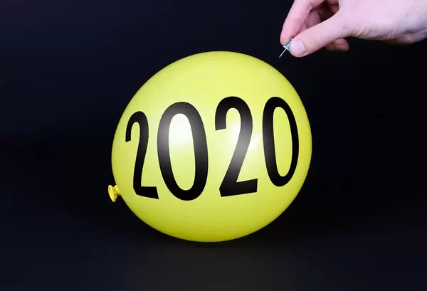 Hand uses a needle to burst a yellow balloon with 2020 text