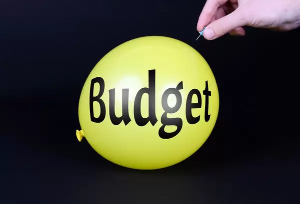 Hand uses a needle to burst a yellow balloon with Budget text