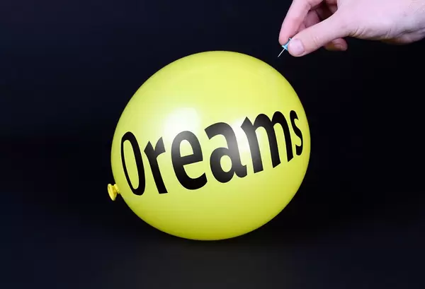 Hand uses a needle to burst a yellow balloon with Dreams text
