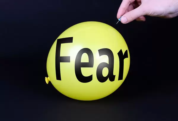 Hand uses a needle to burst a yellow balloon with Fear text