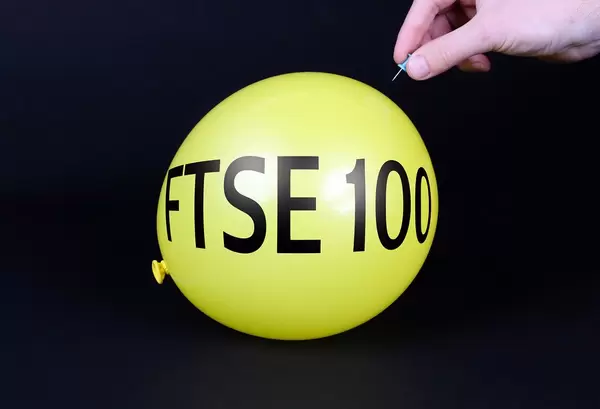 Hand uses a needle to burst a yellow balloon with FTSE 100 text