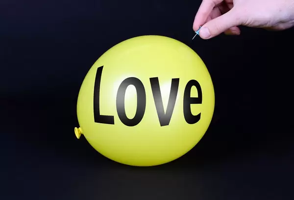 Hand uses a needle to burst a yellow balloon with Love text