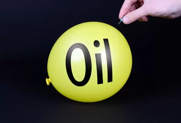 Hand uses a needle to burst a yellow balloon with Oil text