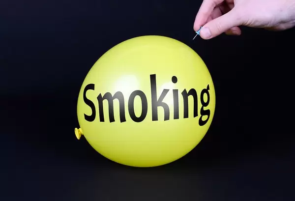 Hand uses a needle to burst a yellow balloon with Smoking text