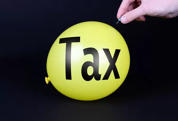 Hand uses a needle to burst a yellow balloon with Tax text