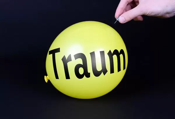 Hand uses a needle to burst a yellow balloon with Traum text