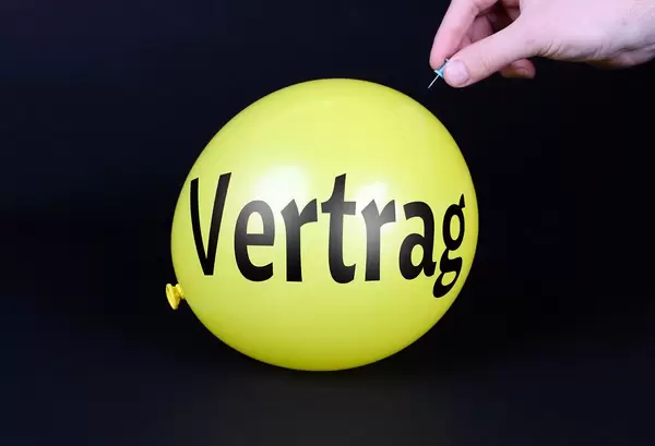 Hand uses a needle to burst a yellow balloon with Vertrag text