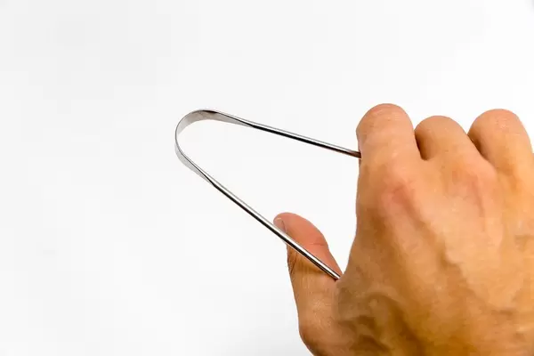 Hand uses the YogaMedic Tongue Scraper made of stainless steal, for oral hygiene, in front of white background
