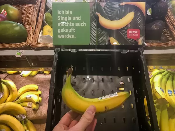 Hand von einem Kunden, der eine einzel verkaufte Banane bei Rewe kauft. Die Kampagne läutet "Ich bin Single und möchte auch gekauft werden"