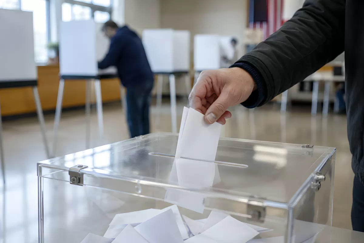 Hand wirft Stimmzettel in transparente Wahlurne