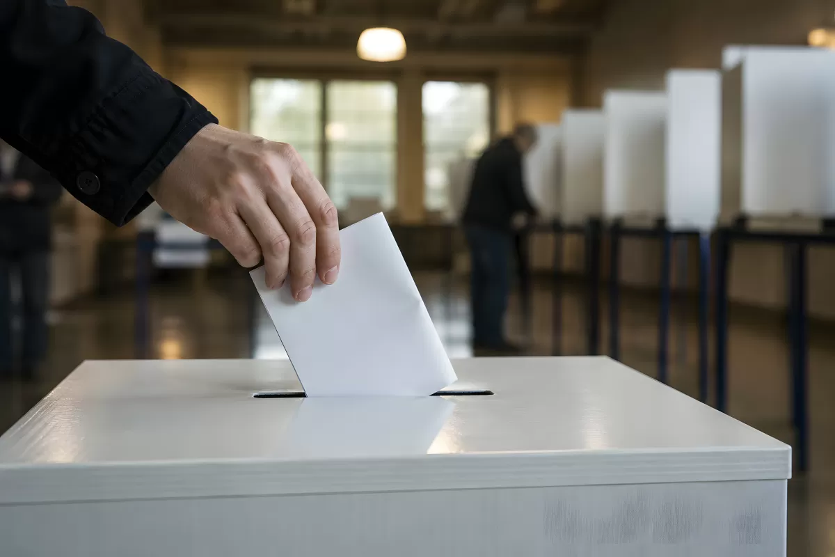 Hand wirft Stimmzettel in weiße Wahlurne