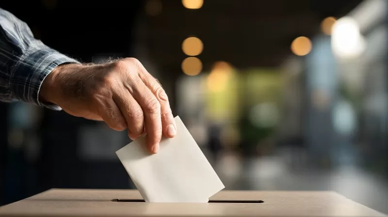 Hand wirft Wahlzettel in Wahlurne bei Stimmabgabe