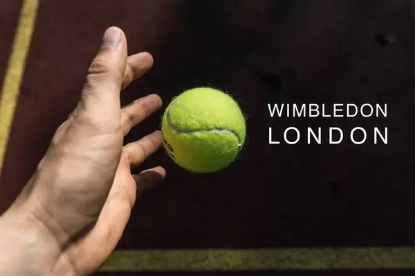 Hand wirft zum Aufschlag einen Tennisball, neben dem Namen des britischen Tennisturniers "Wimbledon London"