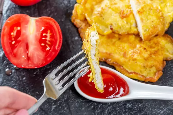 Hand with a fork dips a piece of chop into red tomato sauce