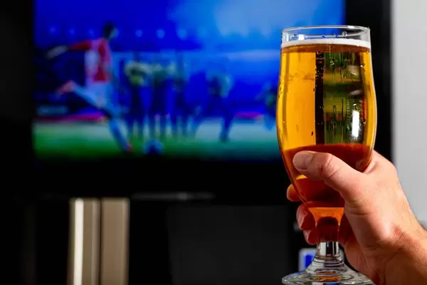 Hand with a glass of light beer on a blurred background of a football match