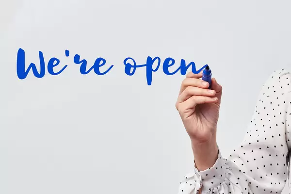 Hand with blue marker writing - We are open