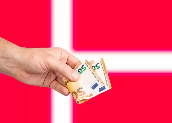 Hand with Euro banknotes over flag of Denmark