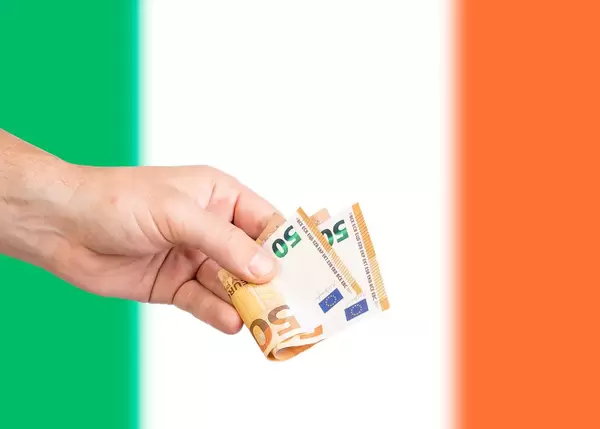 Hand with Euro banknotes over flag of Ireland