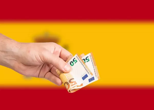 Hand with Euro banknotes over flag of Spain