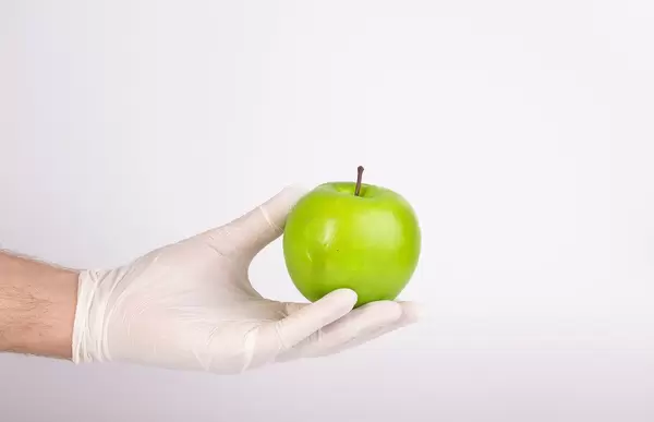 Hand with gloves holding green apple