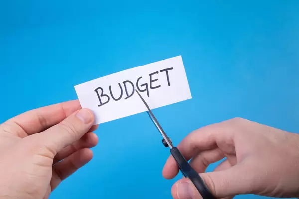 Hand with scissors cutting a paper with Budget text
