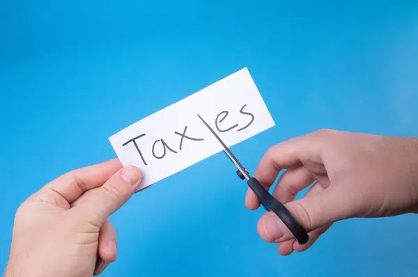 Hand with scissors cutting a paper with Taxes text