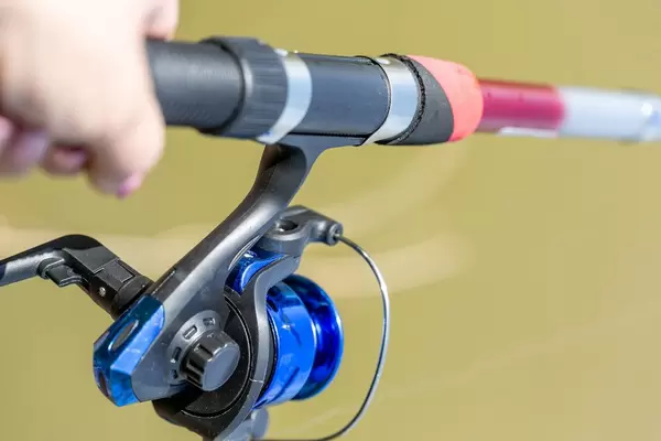 Hand with spinning and reel on the summer lake