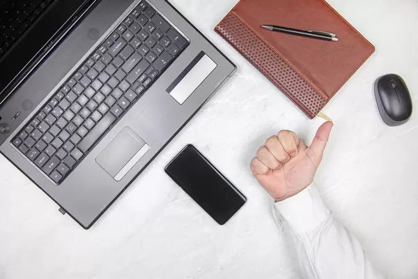 Hand with thumb up on the table with lap top mobile phone and diary