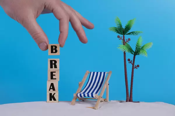 Hand with wooden blocks wiht Break text and beach chair on blue background