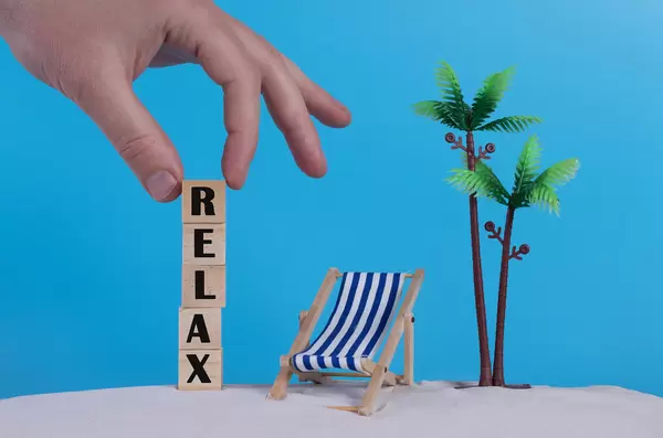 Hand with wooden blocks wiht Relax text and beach chair on blue background