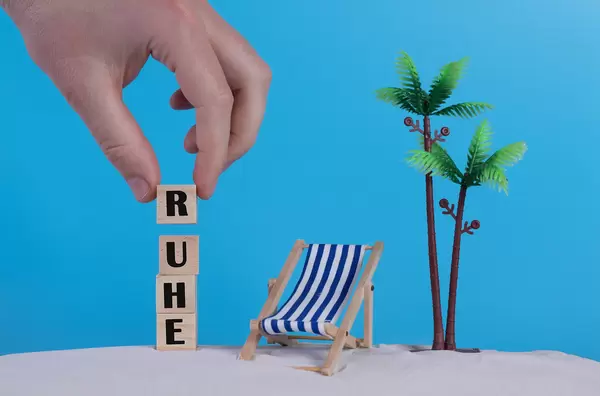 Hand with wooden blocks wiht Ruhe text and beach chair on blue background