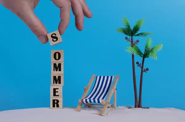 Hand with wooden blocks wiht Sommer text and beach chair on blue background