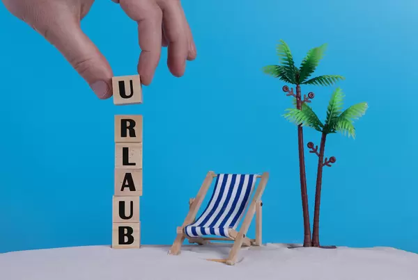 Hand with wooden blocks wiht Urlaub text and beach chair on blue background