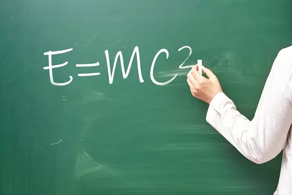 Hand writing well-known E=mc2 physical formula on chalkboard