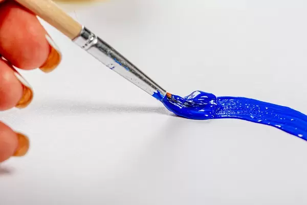 Hand zeichnet einen blauen Streifen mit einem Pinsel auf weiße Oberfläche