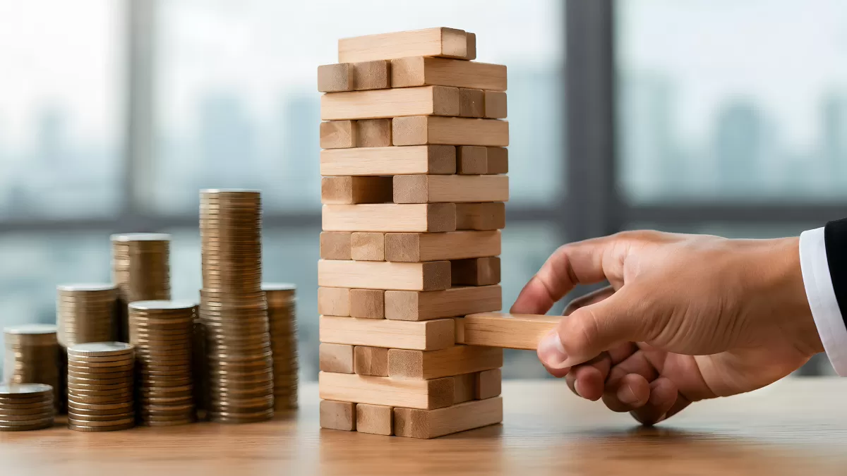Hand zieht Jenga-Stein aus wackeligem Holzturm