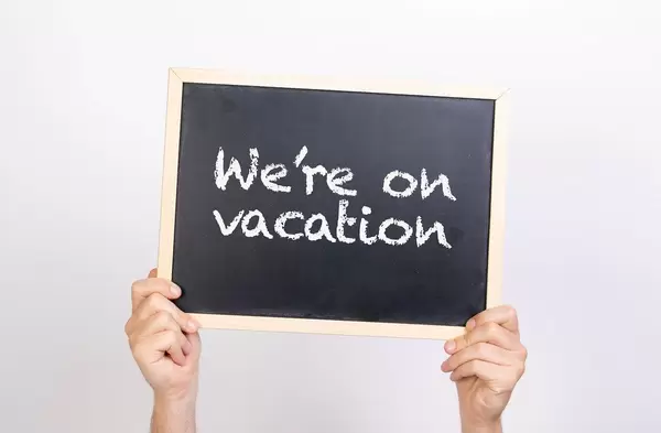 Hände halten eine Kreidetafel hoch, mit dem Hinweis "We're on vacation" - Wir machen Urlaub