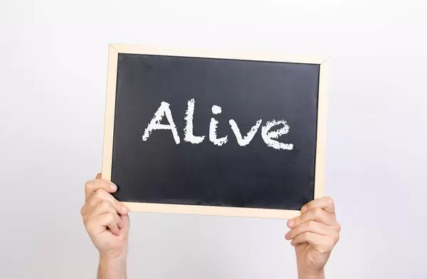 Hände halten eine Kreidetafel hoch, mit dem Text "Alive" - Am Leben