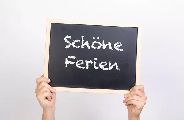 Hände halten eine Kreidetafel hoch, mit dem Text "Schöne Ferien"