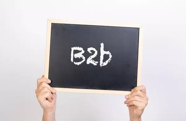 Hände halten eine Kreidetafel hoch, mit der Abkürzung "B2b" (Business to Business) -  Geschäftsbezeichnung zwischen zwei Unternehmen