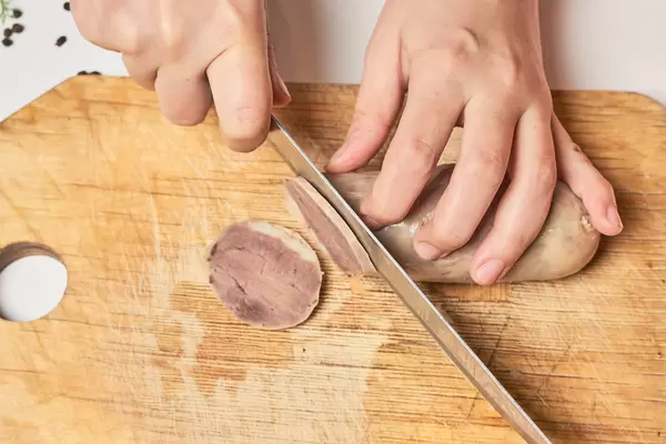 Hände mit Messer schneiden Wurst auf einem Holzbrett. Pferdefleisch Kazy aus Zentralasien