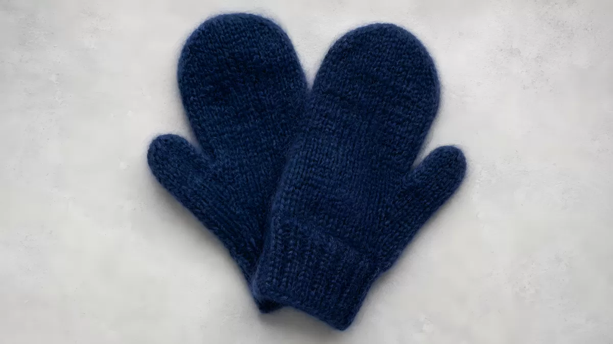 Handgestrickte blaue Fäustlinge auf hellem Untergrund