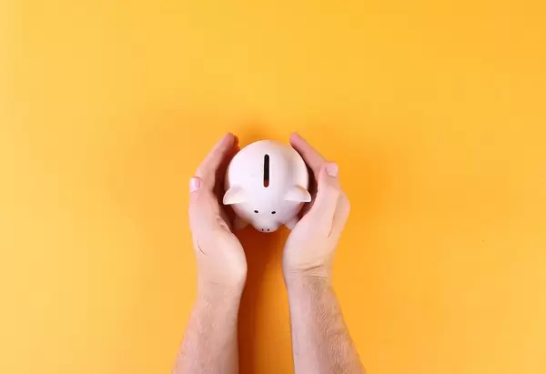 Hands covering piggy bank on orange background