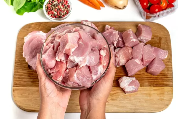 Hands holding a glass bowl with chopped pieces of raw meat, top view