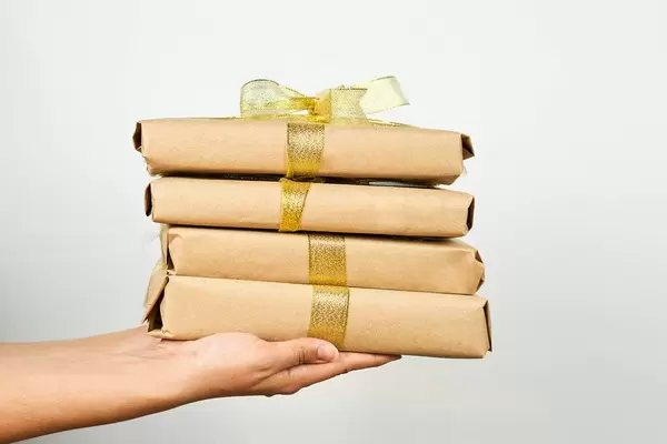 Hands holding a stack of brown paper packages tied with ribbon