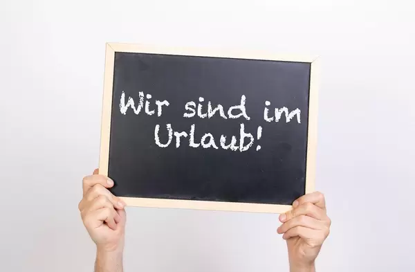 Hands holding blackboard with text Wir sing im Urlaub!