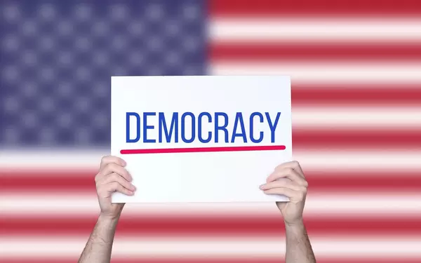 Hands holding board with Democracy text with USA flag background