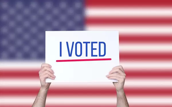 Hands holding board with I Voted text with USA flag background